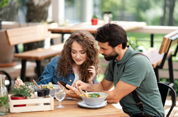 istock Happy couple sitting outdoors on terrace restaurant, using smartphone. 1252592523