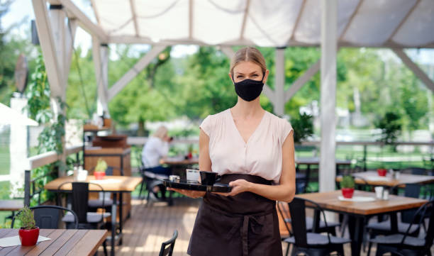 cameriera con maschera facciale che serve i clienti all'aperto sul ristorante sulla terrazza. - starbucks women walking restaurant foto e immagini stock