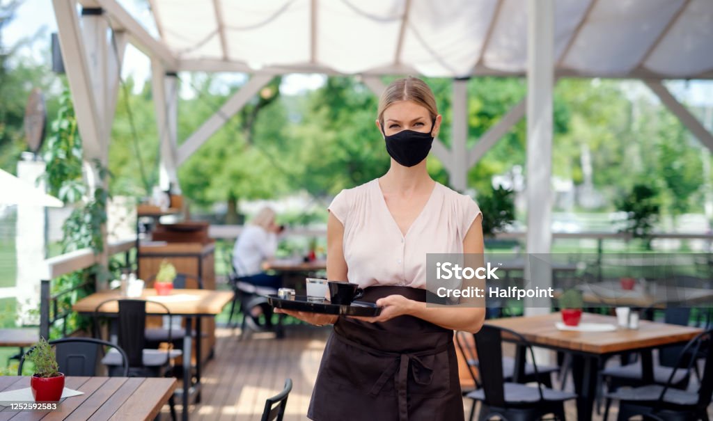 帶面罩的女服務員在戶外露台餐廳為顧客服務。 - 免版稅餐廳圖庫照片