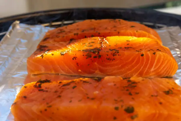 Seasoned raw salmon fish steaks on foil on a grill ready for cooking viewed from the side