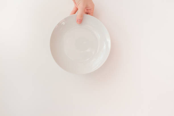 istock Female hand holds a white round plate on a white background as a mockup with copy space. Ceramic flat saucer 1252593726