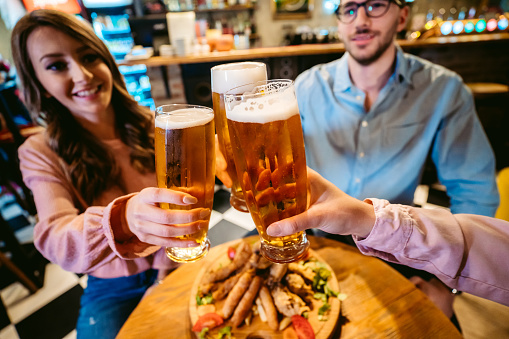 Small group of young Caucasian friends having a nice time talking, drinking beer and eating pub food.