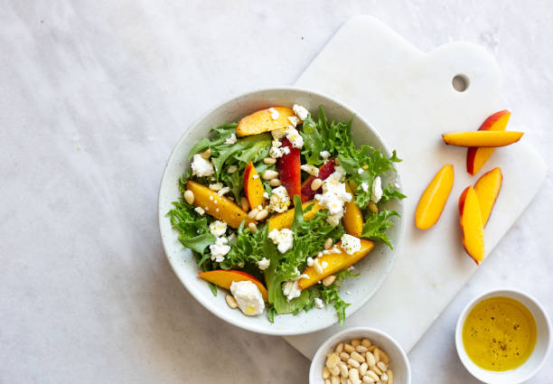 salade d’automne de laitue iceberg, épinards, pêche et fromage de chèvre dans une plaque rustique blanche sur fond de marbre avec l’espace de copie - peach nectarine portion fruit photos et images de collection