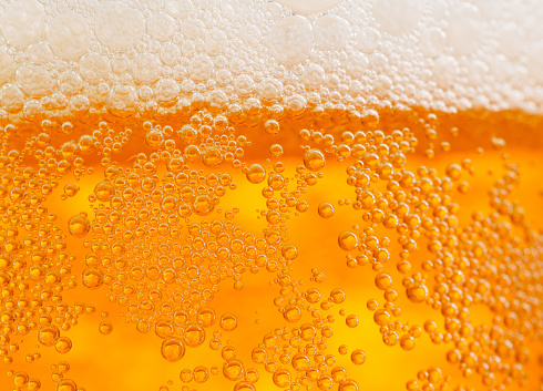 A macro close up abstract image of a cold glass of beer with amber liquid with drops of condensation and bubbles of foamy head.  Shot with a shallow depth of field. 