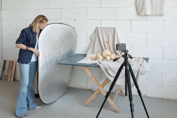 Using lighting reflector Mature photographer in denim outfit adjusting lighting reflector while preparing for photo shoot of food composition reflector stock pictures, royalty-free photos & images
