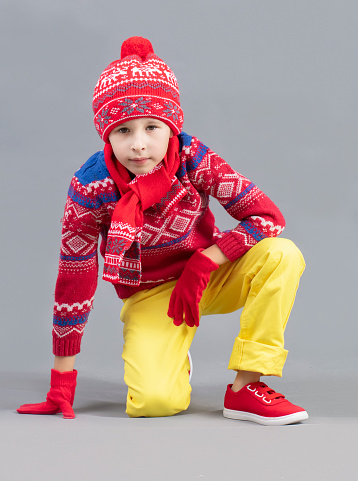 A child in warm clothes. A boy in a red hat and sweater and sneakers. Fashionable boy in the studio.
