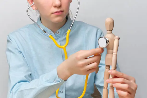 Doctor abstractly listens to the heart of a mannequin through a stethoscope. Close up.