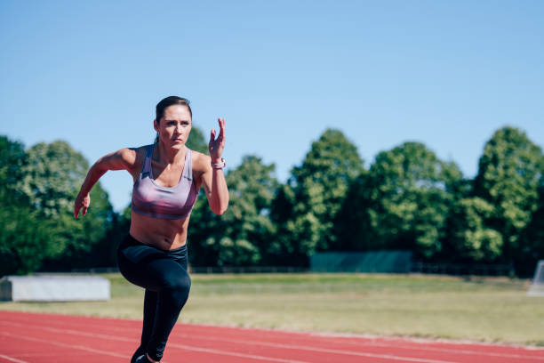 Mid adult Caucasian female athlete sprinting on sports track Front view of focused female athlete in early 30s wearing sports bra and tights sprinting during training session on outdoor sports track. woman sprint stock pictures, royalty-free photos & images