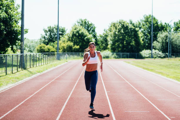 atleta femenina adulta media acercándose a la cámara en el carril central - pista de atletismo de tartán fotografías e imágenes de stock