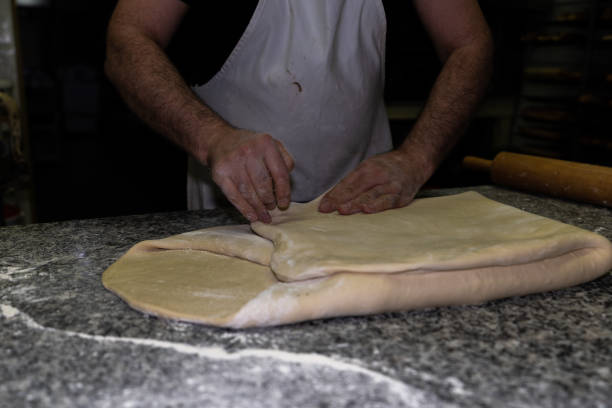 fornaio piegando l'impasto croissant per allungarlo di nuovo e mescolare bene gli ingredienti in una pasticceria - triangle human hand house home interior foto e immagini stock