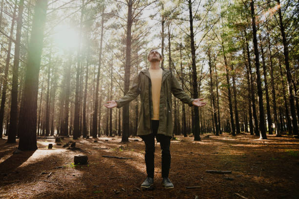 joven macho tomando en los alrededores del bosque, respiraciones profundas y conexión religiosa con la naturaleza - praying forest freedom tree fotografías e imágenes de stock