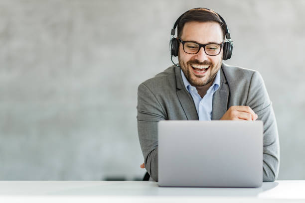 Happy businessman having a video call over laptop in the office. Happy male entrepreneur with headphones talking to someone during conference call over a computer in the office. Copy space. web conference photos stock pictures, royalty-free photos & images