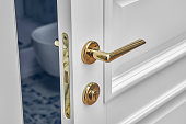 Classic style white door. Classic white door with golden handle. Opened white door to the bathroom. Close-up