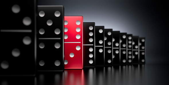 Black and one red domino tiles in a row falling with dark background