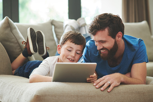 Shot of an adorable little boy using a digital tablet with his father on the sofa at home
