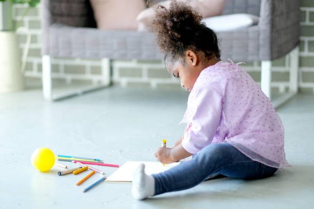 istock Little African American enjoy with writing or drawing by colored pencils on notebook put on the floor in living room. Concept of good creativity occur during children learning from home 1252670448