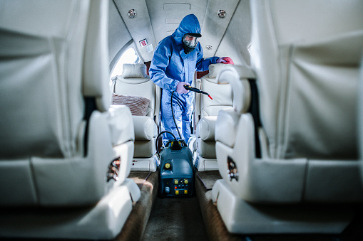 A man in coveralls cleaning seats in a private airplane during a COVID-19 pandemic.