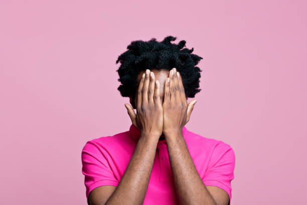 homem vestindo camisa polo rosa cobrindo o rosto com as mãos - polo shirt african ethnicity men african descent - fotografias e filmes do acervo