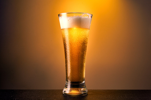 Cold craft light Beer in a glass with drops on a dark table. Pint of Beer on yellow color background. Close up.
