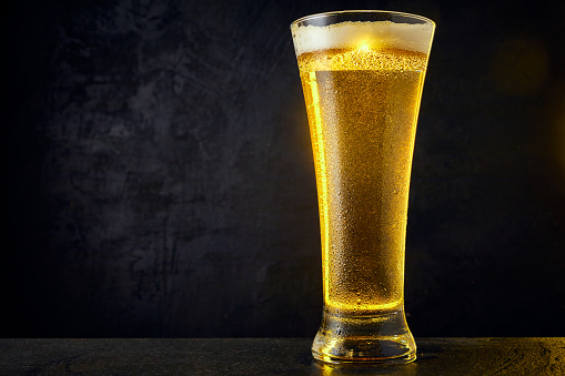 Cold craft light Beer in a glass with drops on a dark table. Pint of Beer on black color background. Close up.