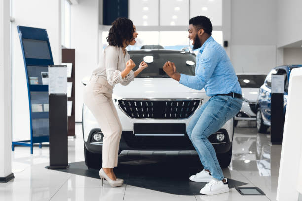 ディーラーで新しいオートの近くに立っている拳を振る興奮した配偶者 - car african descent shopping car dealership ストックフォトと画像