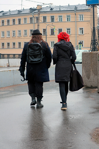 April 10, 2019, Russia, St. Petersburg, a man with long hair in a hat with an unopened umbrella in his hand and a woman with red hair are walking in the rain