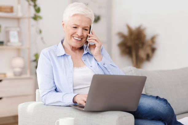 istock Modern senior lady working on laptop and talking on cellphone at home 1252686713