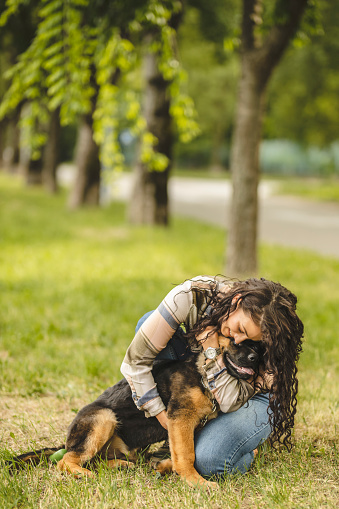 Happy young woman playing with her German Shepherd dog on the grass in park