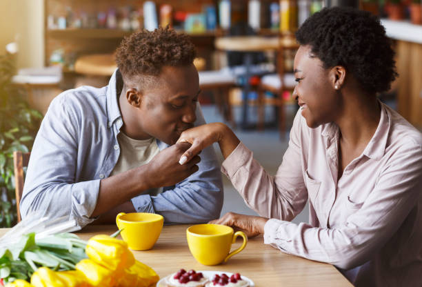 l'uomo afroamericano bacia la mano della sua amata ragazza a tavola nel caffè moderno - couple black american culture kissing foto e immagini stock