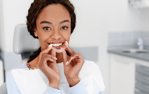 Chica negra sonriente sosteniendo alineador invisible, entrenador de dientes moderno photo