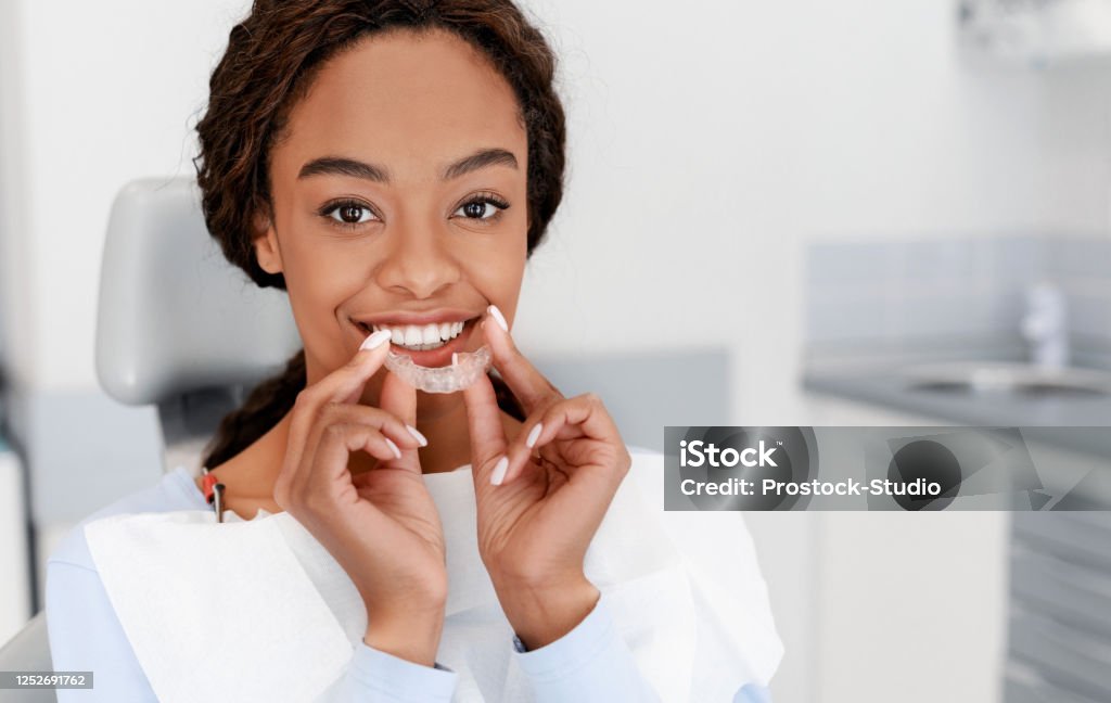 Smiling black girl holding invisible aligner, modern teeth trainer Dental Treatment Concept. Close up of young black woman holding invisible aligner, whitening tray, free space Dental Aligner Stock Photo