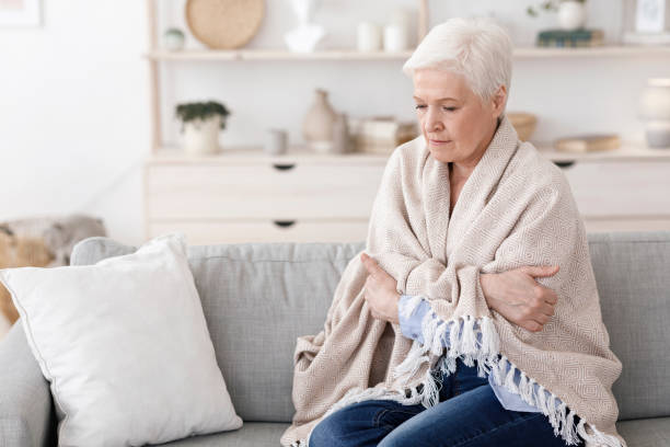 Senior lady sitting on couch covered with blanket, shivering with high temperature Sick senior lady sitting on couch covered with blanket, freezing shivering due to high temperature, suffering from coronavirus at home shivering stock pictures, royalty-free photos & images