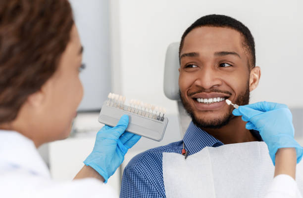 Dentist choosing filling shade for smiling patient Female dentist choosing filling shade for smiling black guy, using tooth scale sample, close up dental cavity photos stock pictures, royalty-free photos & images