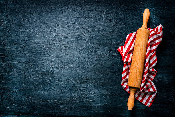 Cooking or kitchen backgrounds: wooden rolling pin on checkered napkin shot from above on black background. The composition is at the right of an horizontal frame leaving useful copy space for text and /or logo. High resolution 42Mp studio digital capture taken with SONY A7rII and Zeiss Batis 40mm F2.0 CF lens