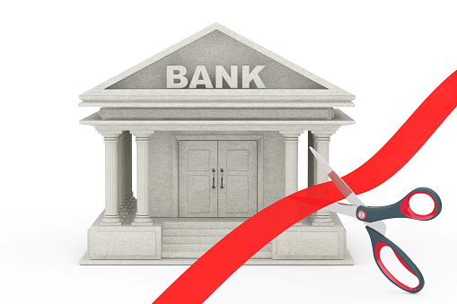 Scissors Cutting Red Ribbon in Front of Bank Building on a white background. 3d Rendering