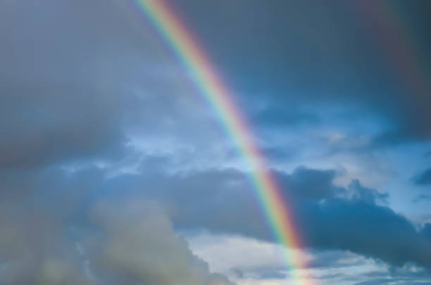 istock Rainbow against the dark blue sky with clouds. Light effect. Drizzling rain. 1252703113