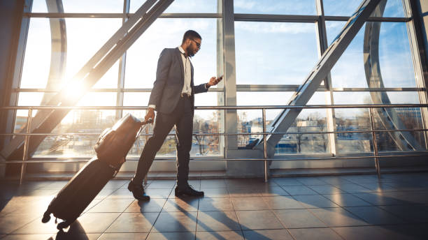 istock Black Businessman Using Mobile Phone Walking In Airport, Panorama, Side-View 1252703573