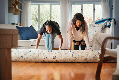 Shot of a two women unrolling carpet in new house