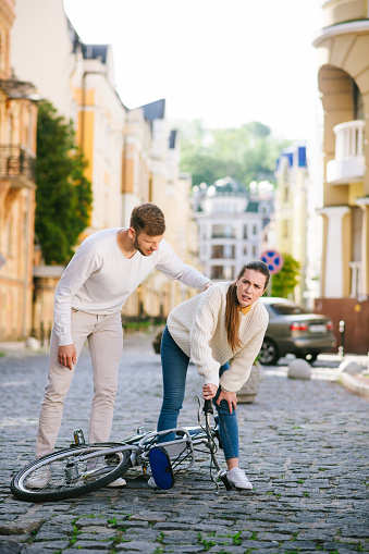 Knee pain. Unhappy woman holding her knee standing over a fallen bicycle and an attentive man nearby.