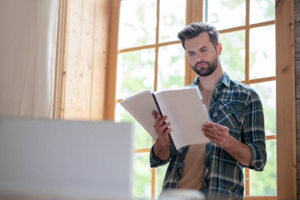 istock Man in a checkered shirt standing in the kitchen holding documents and looking attentive 1252707650