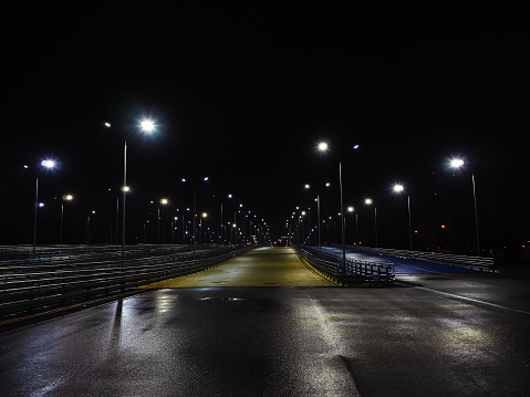 Night view of the roads going into the distance, with fences on the sides and illuminated by lights