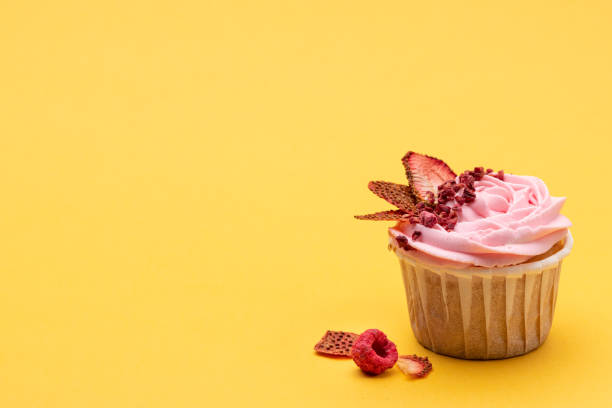 istock Pink cupcake decorated in modern style with sublemented berries on bright yellow background. Horizontal with space for text 1252711698