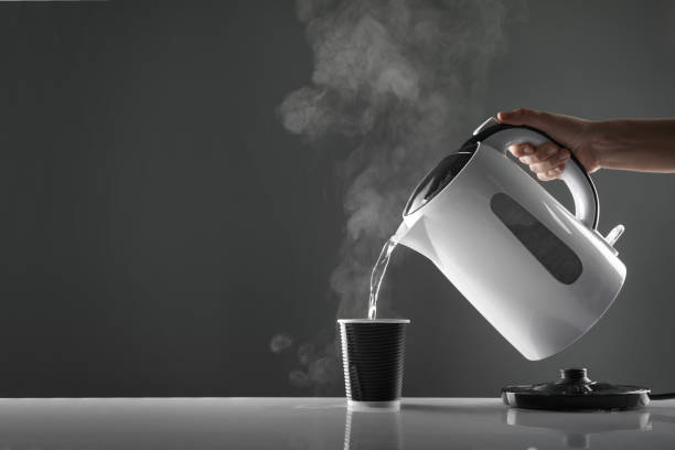 Electric white kettle pouring water in cup on table on grey background Electric white kettle pouring water in cup on table on grey background boiling stock pictures, royalty-free photos & images