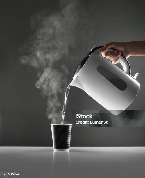 Premium Photo  Kettle pouring boiling water into a cup on grey background.  top view.