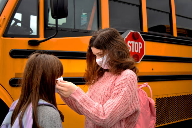 istock Two students assist wearing face masks by a school bus 1252718846