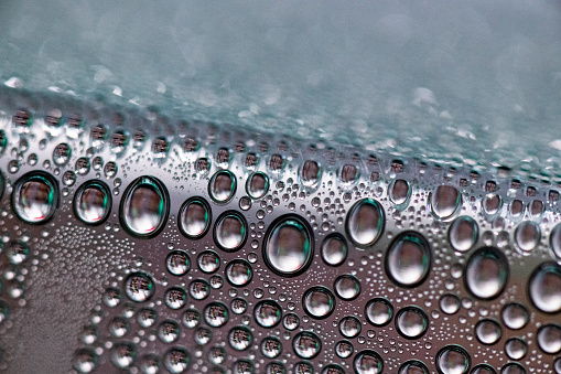 Rain or water drops different size on a black shiny car hood surface. Water droplets on dark iron surface and texture. Abstract background and water texture for design