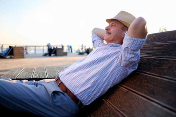 Senior hispanic man in summer hat sitting outdoors on bench. Summer evening time.