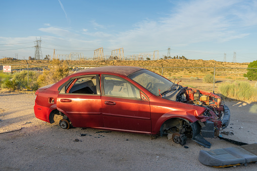 Victorville, CA / USA – May 22, 2020: A red abandoned four door sedan with missing engine and tires in Victorville, California.