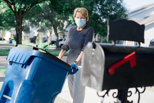 A Senior caucasian woman is taking out the garbage protected with face mask and gloves