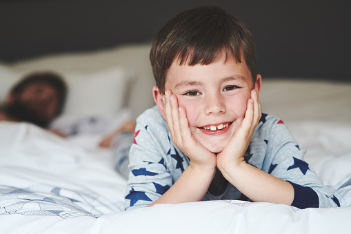 Portrait of an adorable little boy relaxing on the bed with his father in the background